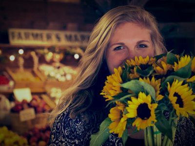 a woman smiles behind a bouquet of sunflowers